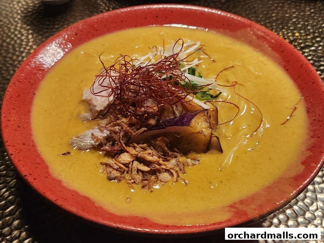 A close-up of a vibrant yellow soup with meat, eggplant, and crispy toppings.