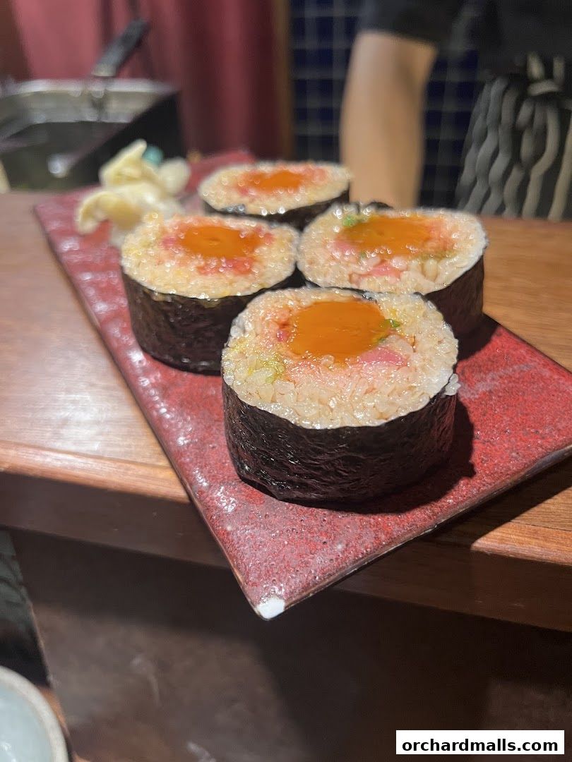 A plate of four sushi rolls with a bright orange topping and pickled ginger.