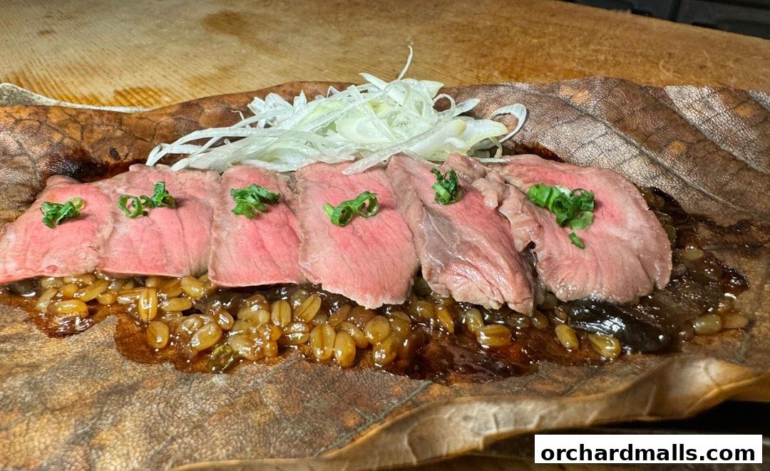 Thinly sliced rare beef served over grains on a large leaf.