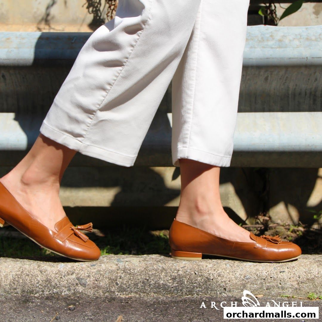 A person wearing white pants and brown tassel loafers walks on a concrete ledge.