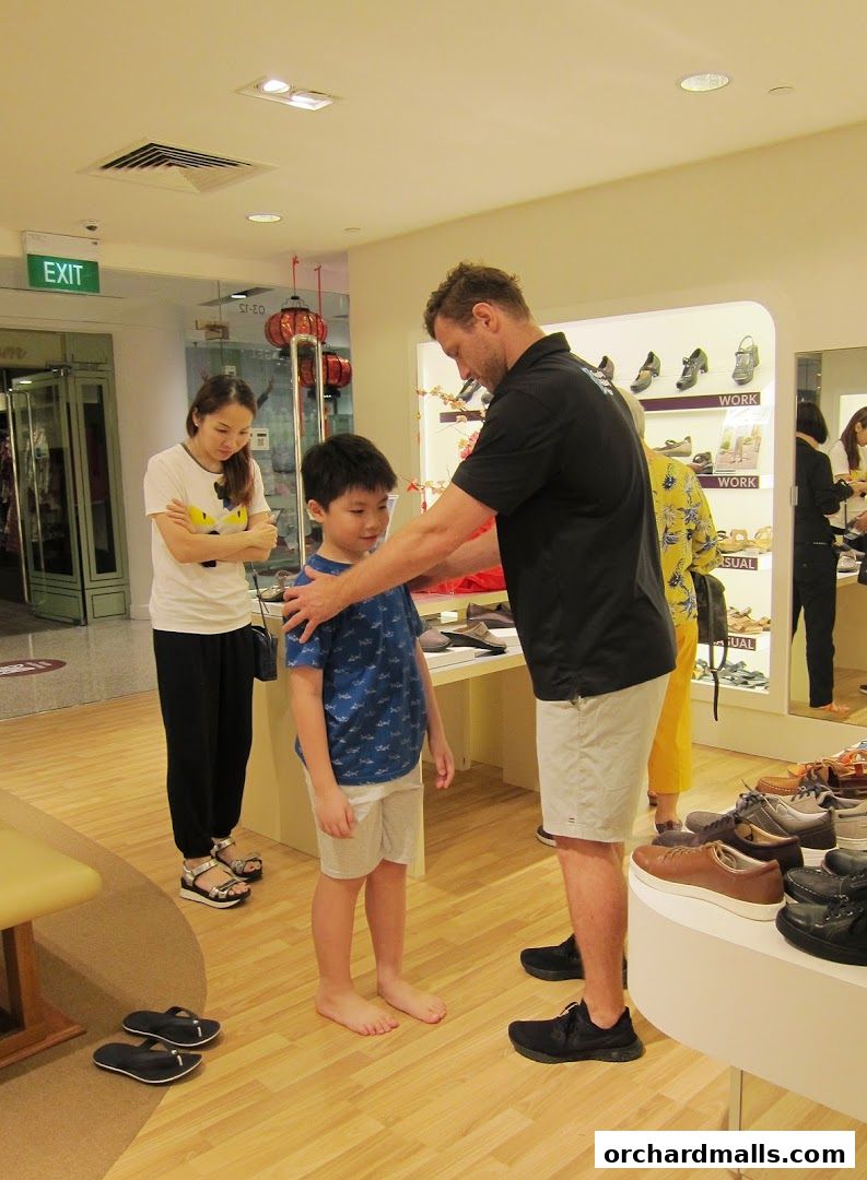 A shoe store employee helps a young boy try on shoes while his mother watches.