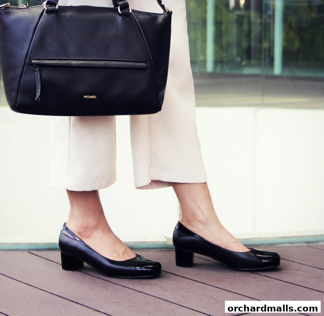 A person wearing black heels and carrying a black handbag.
