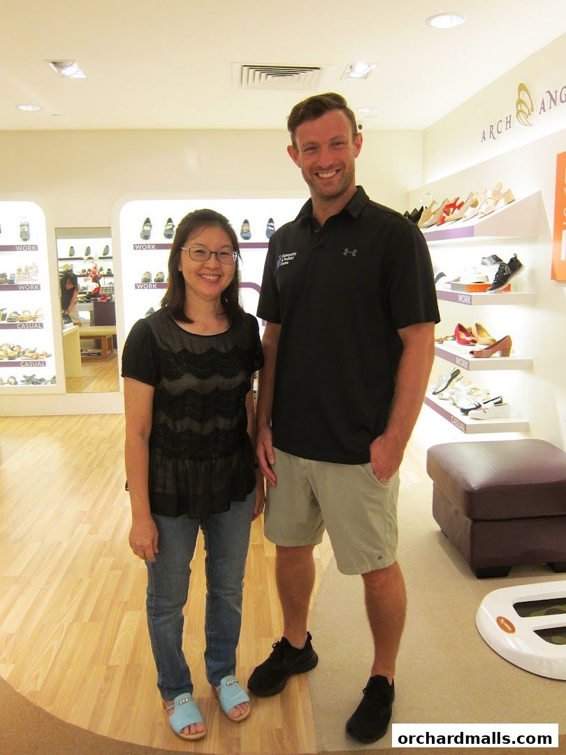A woman and a man smiling in a shoe store with shelves of shoes in the background.