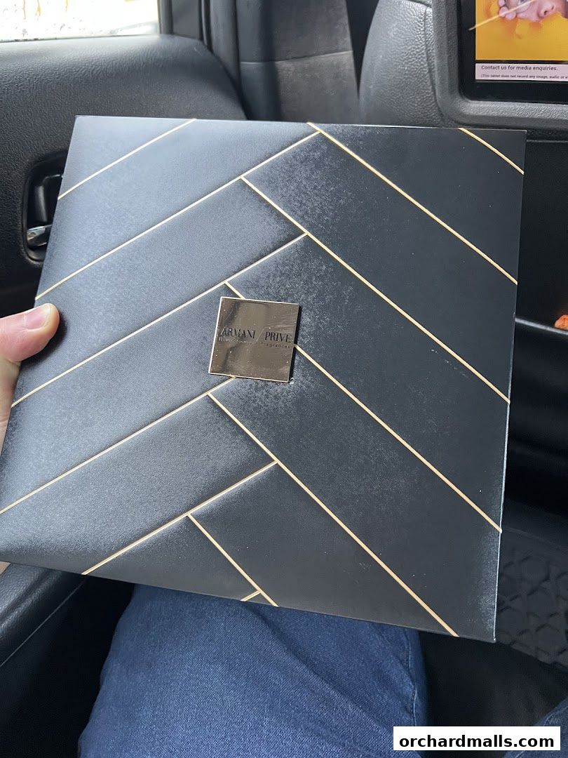 A person holds a black gift box with gold geometric lines and an Armani Prive logo.