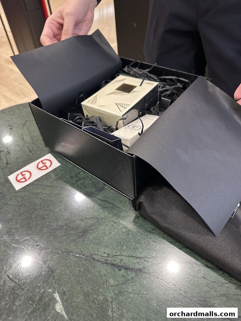 Hands opening a black gift box filled with Armani beauty products and tissue paper.