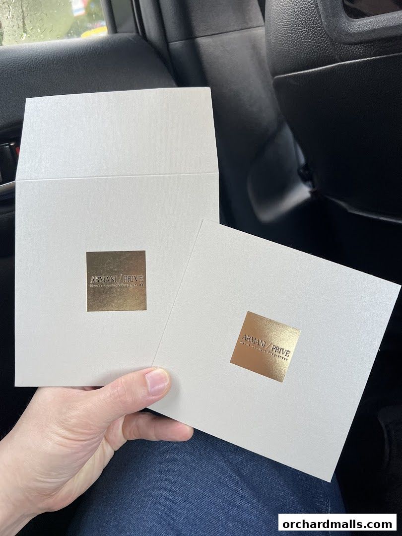 A hand holds two white envelopes with the Armani Privé logo in gold.