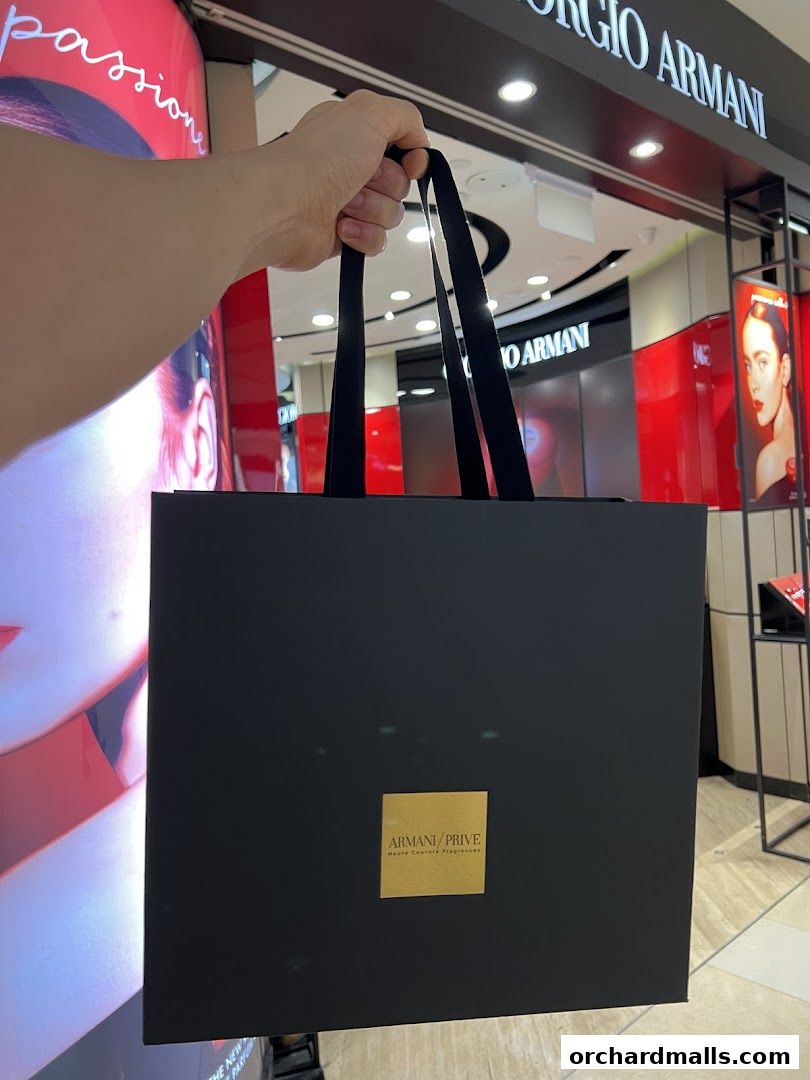 A person holds a black Armani beauty shopping bag in front of the store.