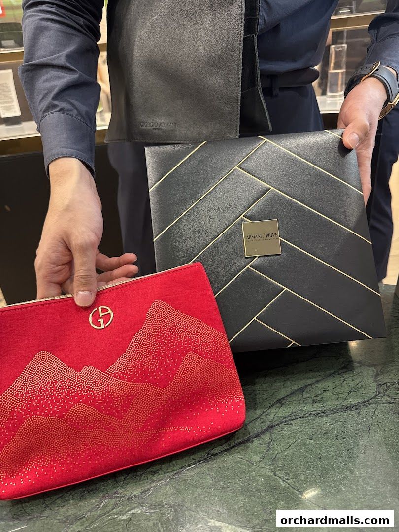 A person holds a red cosmetic bag and a black gift box from Armani Beauty.