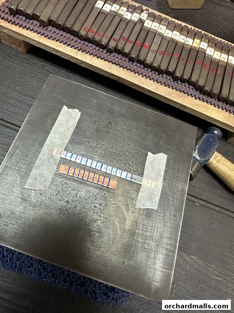 Metal stamping tools and a piece of metal being engraved with letters.