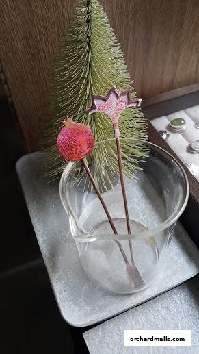 Artisan cocktail stirrers shaped like a pomegranate and a flower in a beaker.