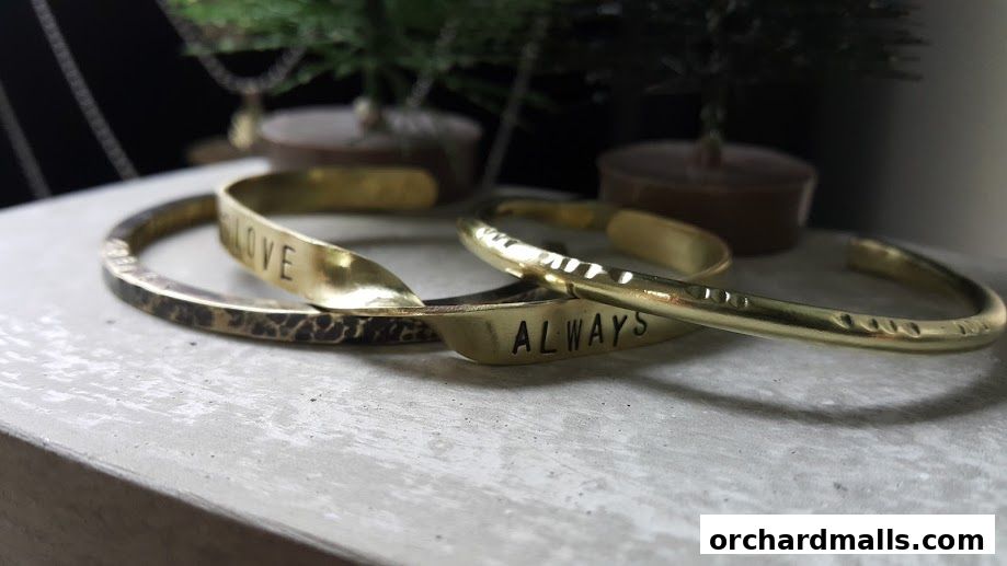 Close-up of four brass bracelets with engraved words and textures.