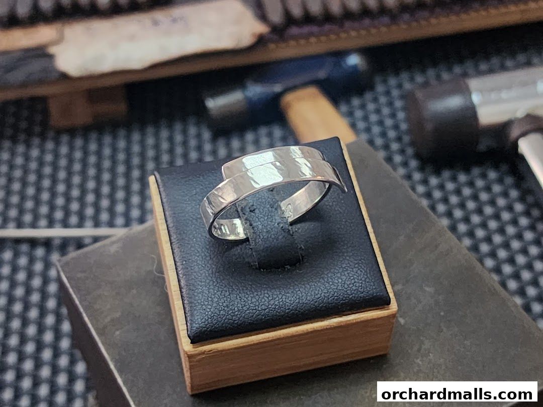 A handcrafted silver ring displayed on a black velvet stand with tools in the background.