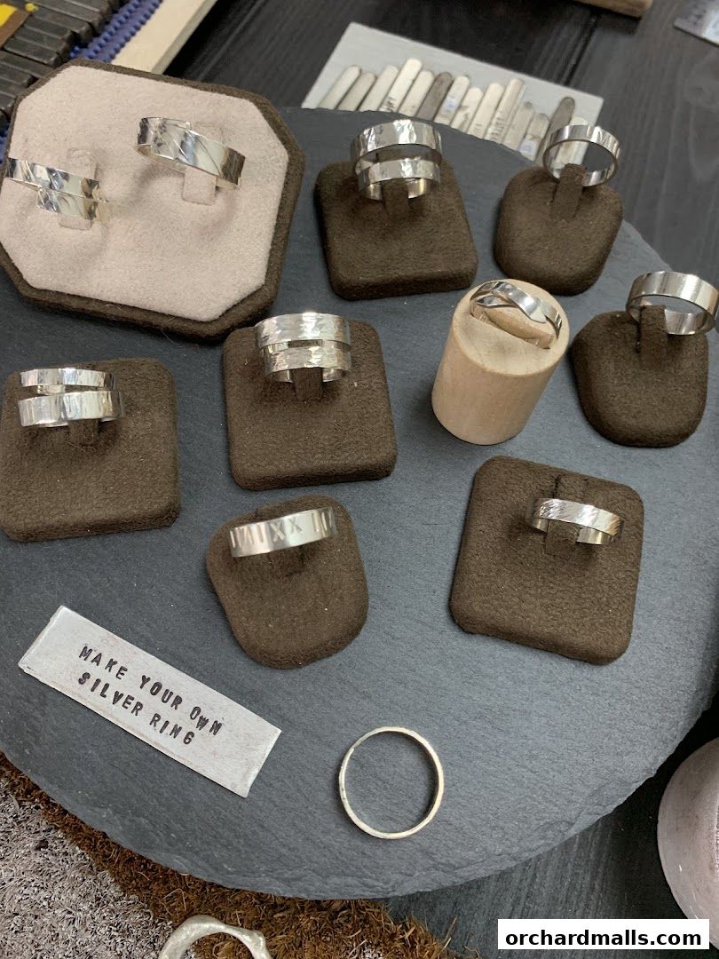 A display of various handcrafted silver rings on stands, with a sign saying 'Make Your Own Silver Ring'.