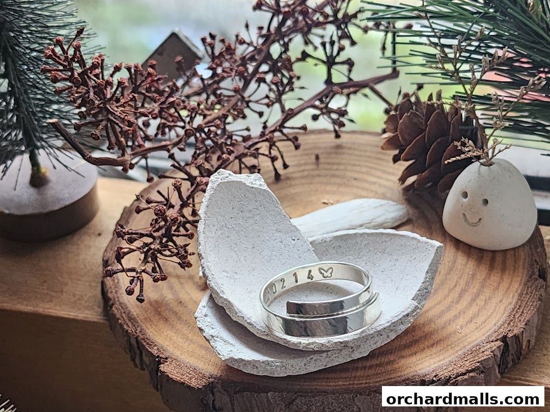 A handcrafted silver ring with stamped numbers and a butterfly rests in a decorative dish.