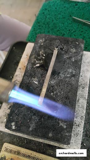 A metal strip is being heated with a torch on a charcoal block.