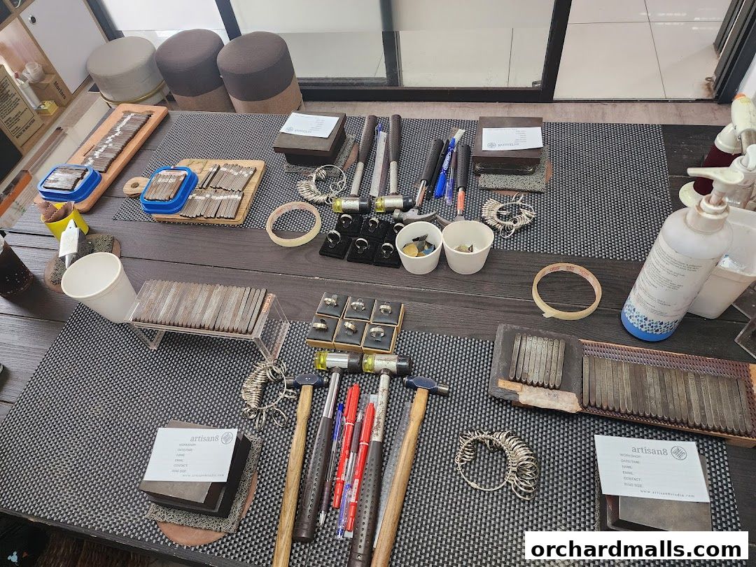 Jewelry making tools and materials laid out on a table, including ring sizers and hammers.