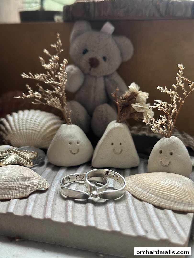 A display of rings, small decorative figures, and seashells, with a teddy bear in the background.