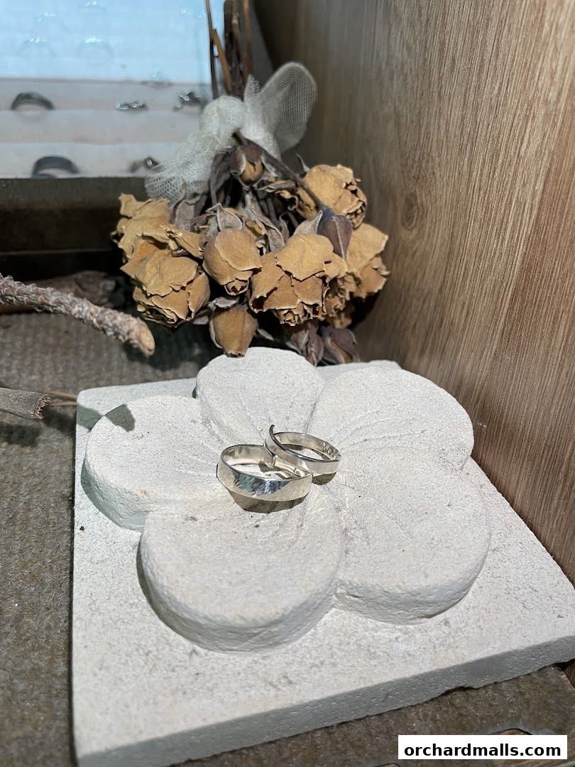 Two silver rings displayed on a decorative stone flower with dried roses.