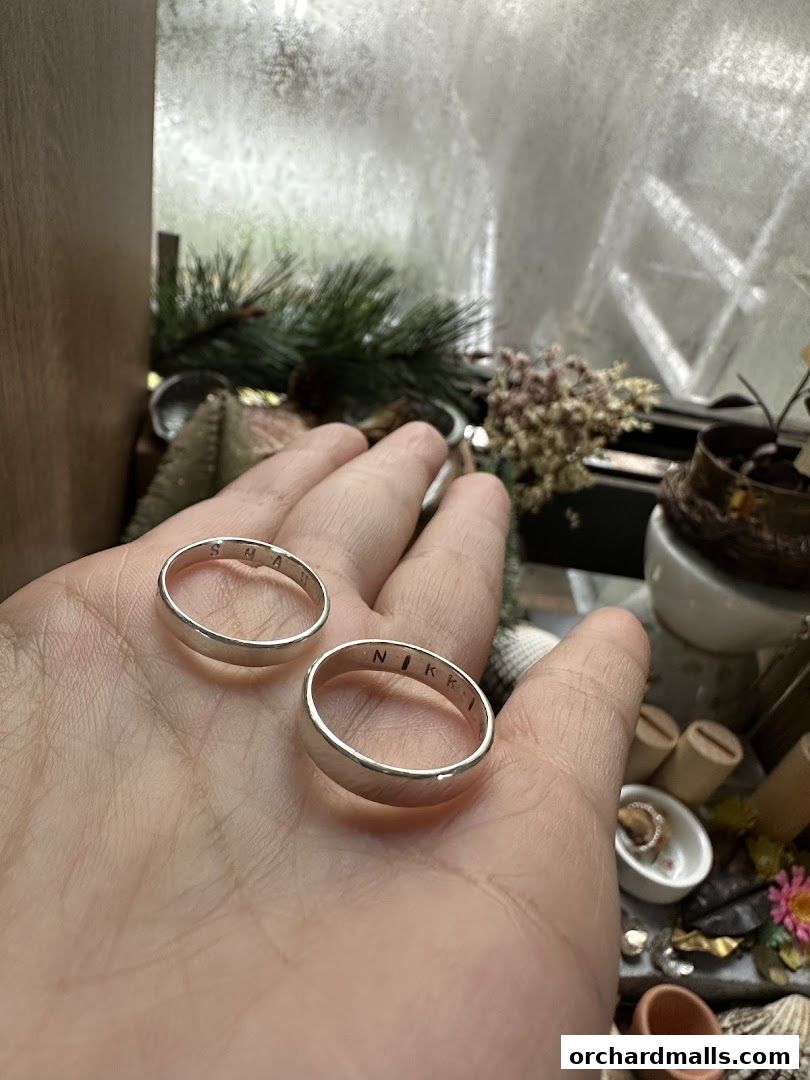 Two personalized silver rings with engraved names held in a hand.