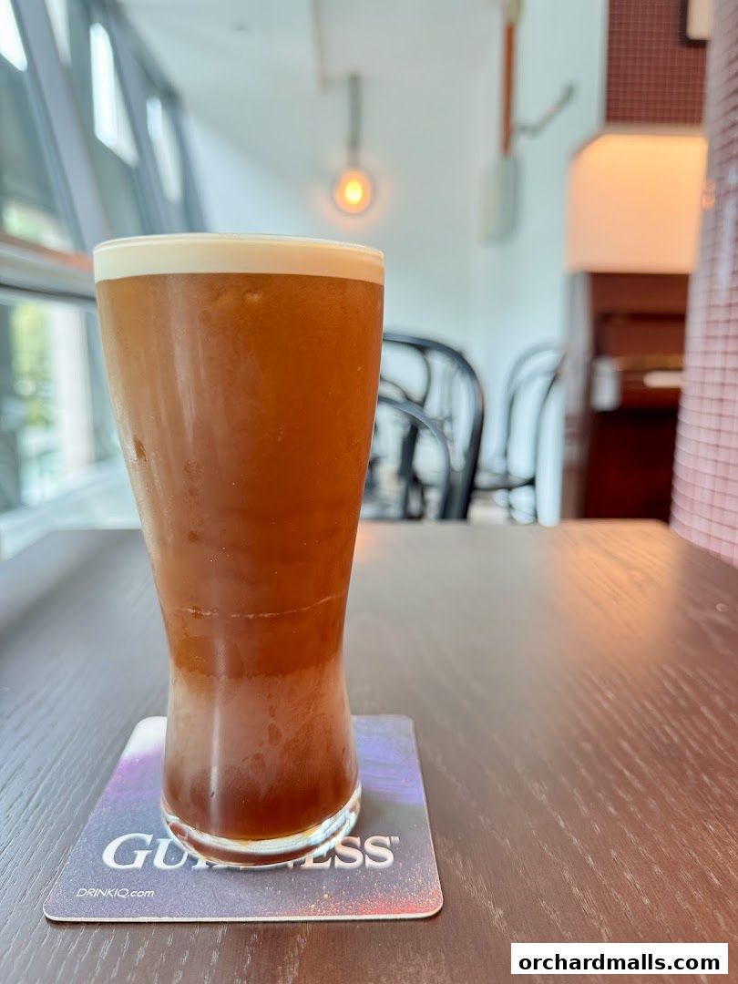 A tall glass of iced coffee with a foamy top sits on a coaster.