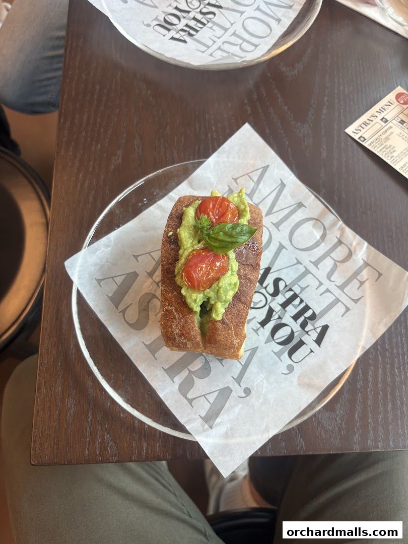 Avocado toast with cherry tomatoes and basil on a branded paper liner.