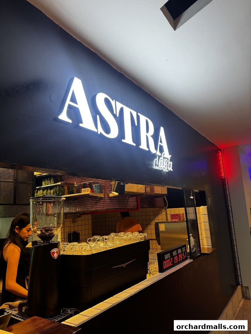 The illuminated sign of ASTRA Deli 星辰咖啡 above a coffee counter with a barista.