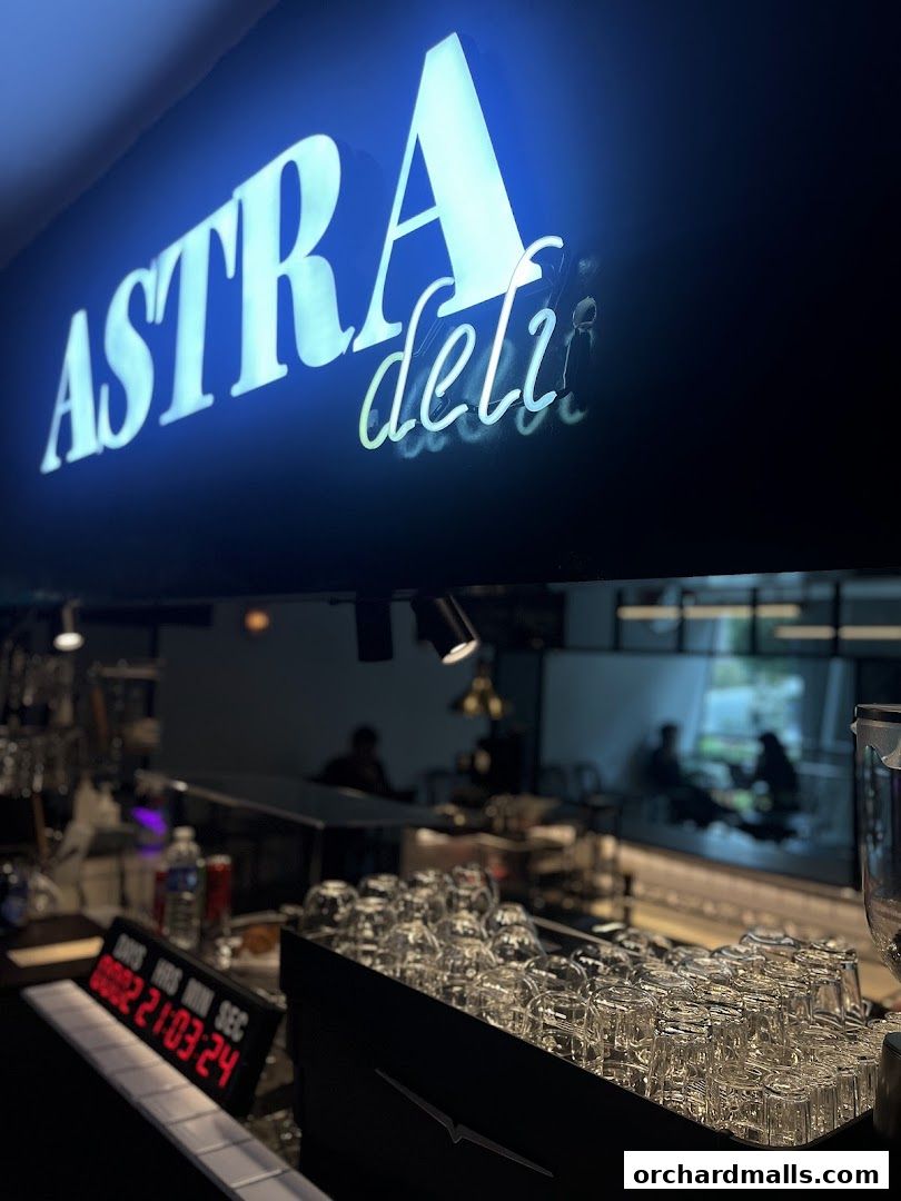 A neon sign for ASTRA Deli is visible above a counter with stacked glasses.