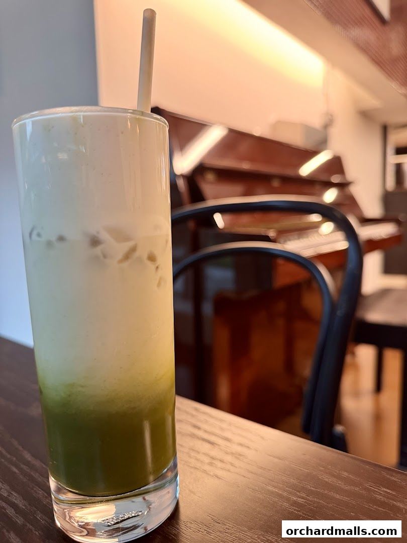 A tall glass of iced matcha latte with a straw on a wooden table.