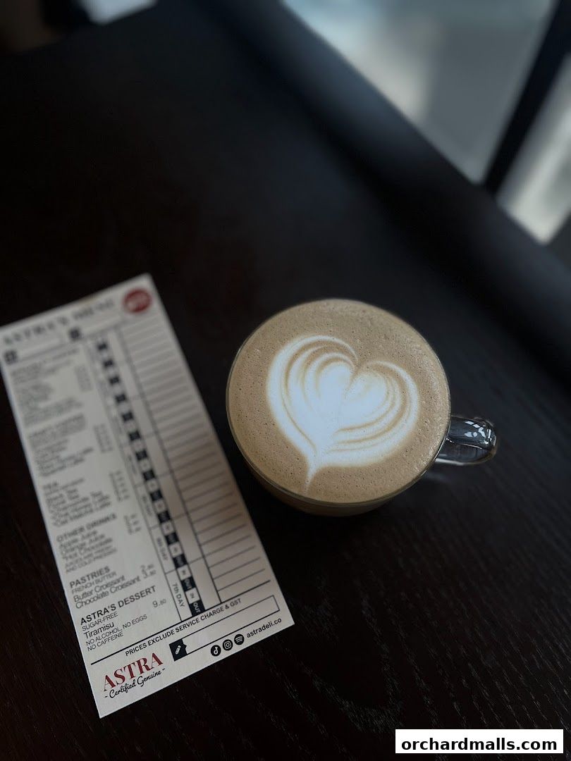 A latte with heart art next to a menu from ASTRA Deli.