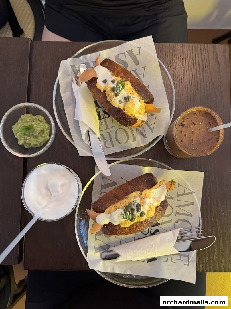 Two gourmet sandwiches with salmon and sauce, served with sides and a drink.