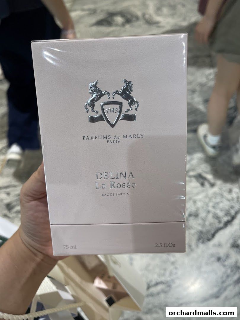 A hand holds a pink box of Parfums de Marly Delina La Rosée Eau de Parfum.