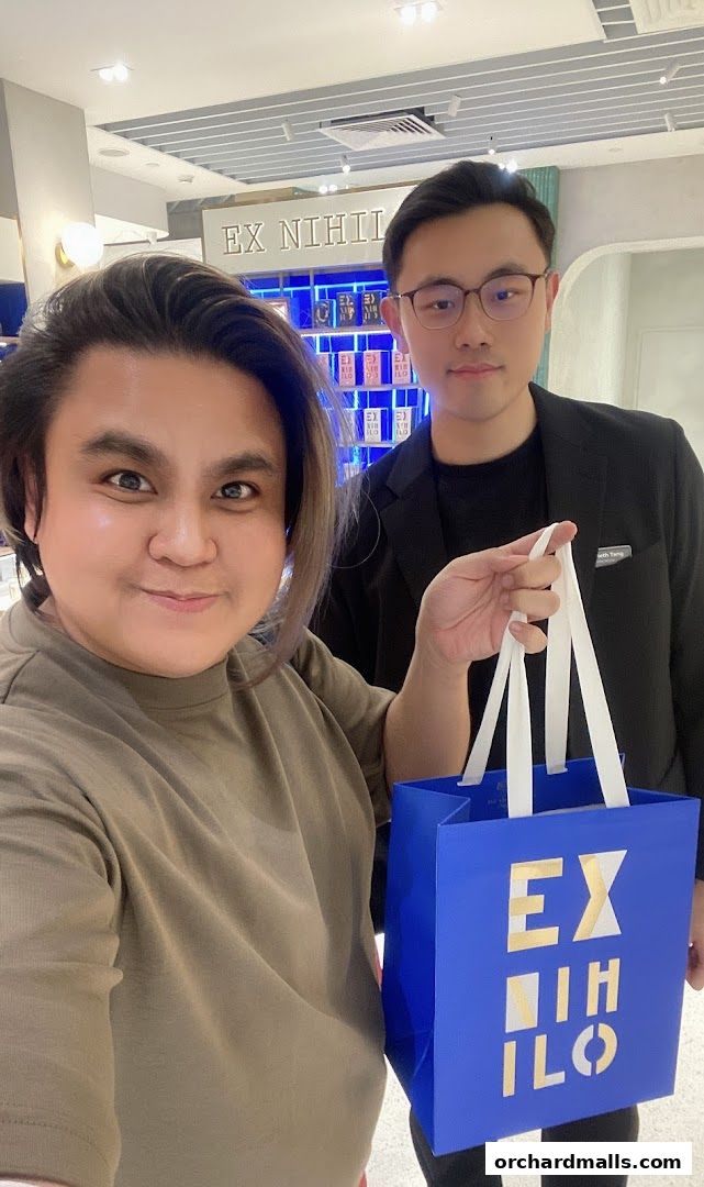 Two people pose with a blue shopping bag from a luxury fragrance store.