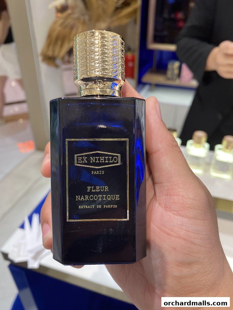 A hand holds a dark blue perfume bottle with a gold cap and label.
