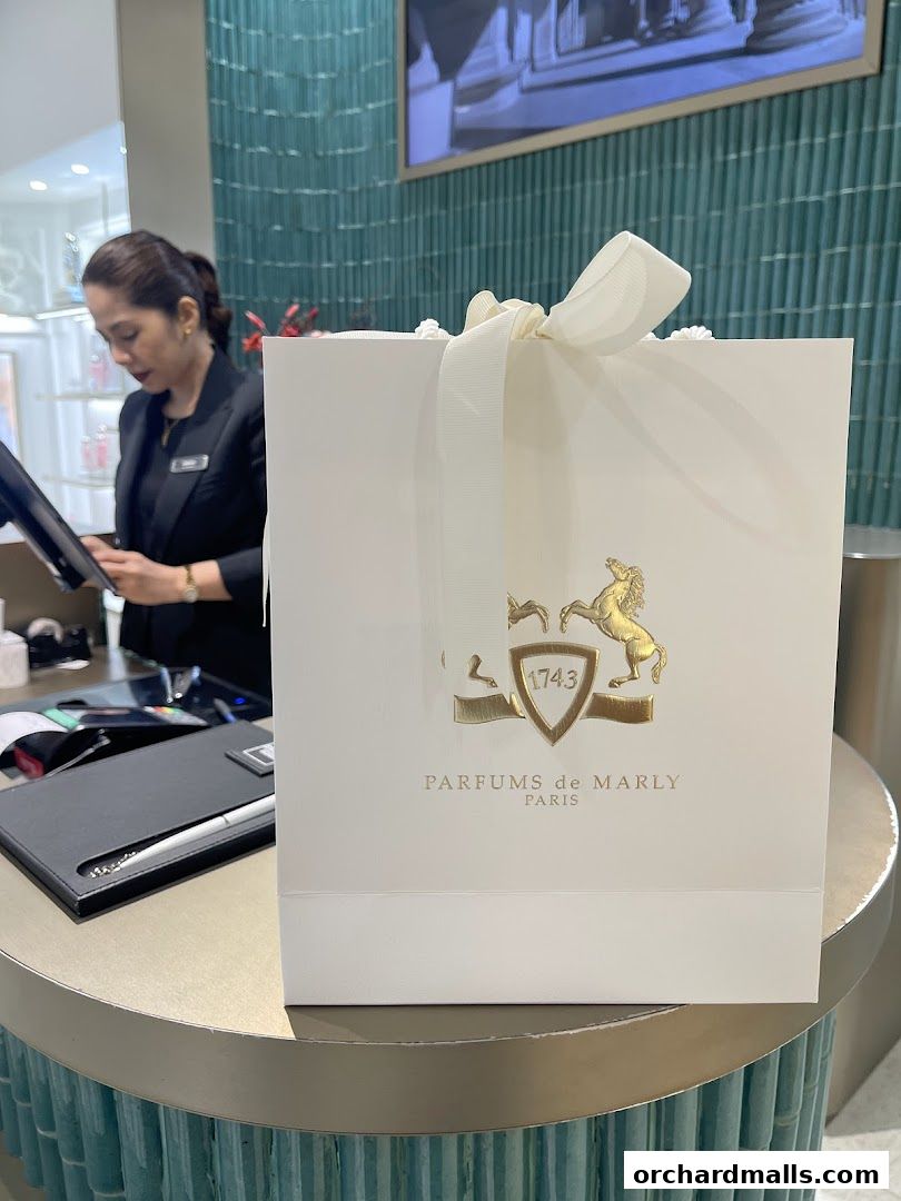 A shopping bag from Parfums de Marly Paris is displayed at a counter with a sales associate.
