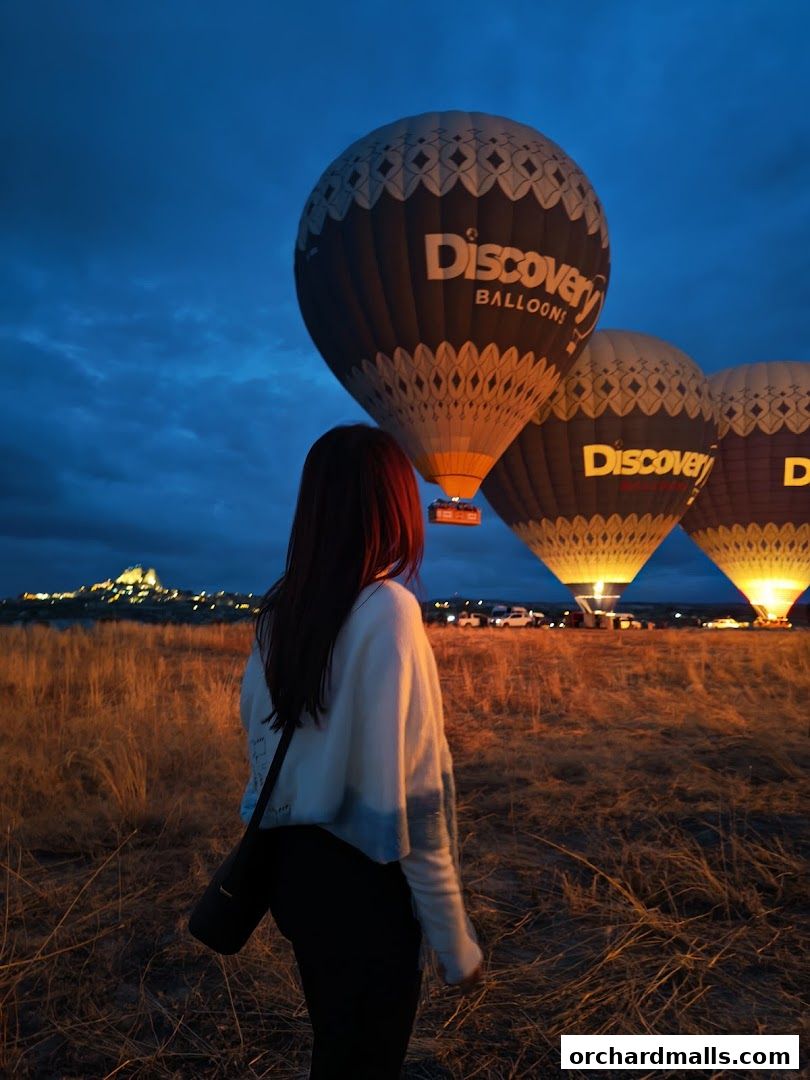 A woman watches hot air balloons inflate at dawn with a distant town.