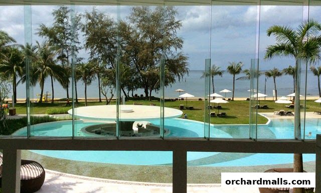 View of a resort pool and beach with palm trees and lounge chairs.