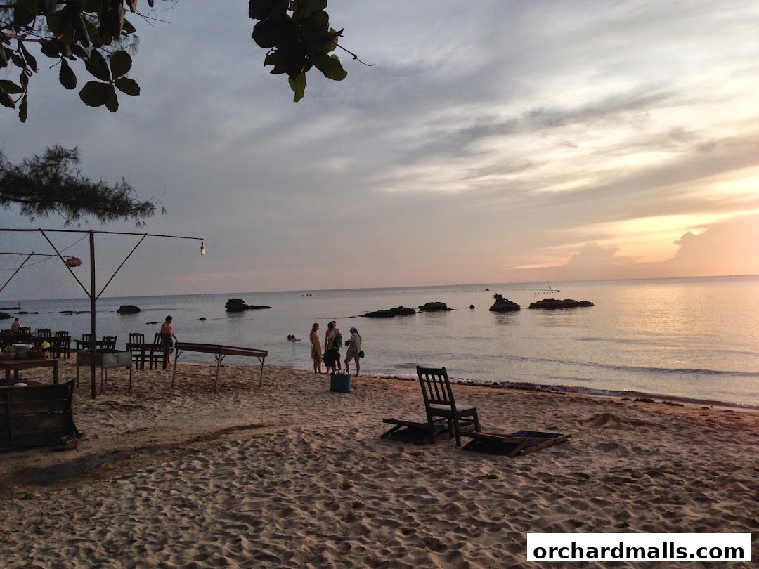 A serene beach scene at sunset with people enjoying the view and outdoor seating.