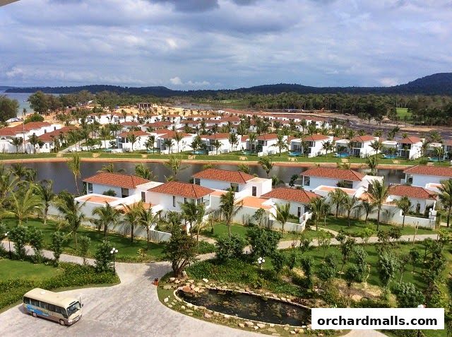 Aerial view of a resort with white villas, palm trees, and a lake.