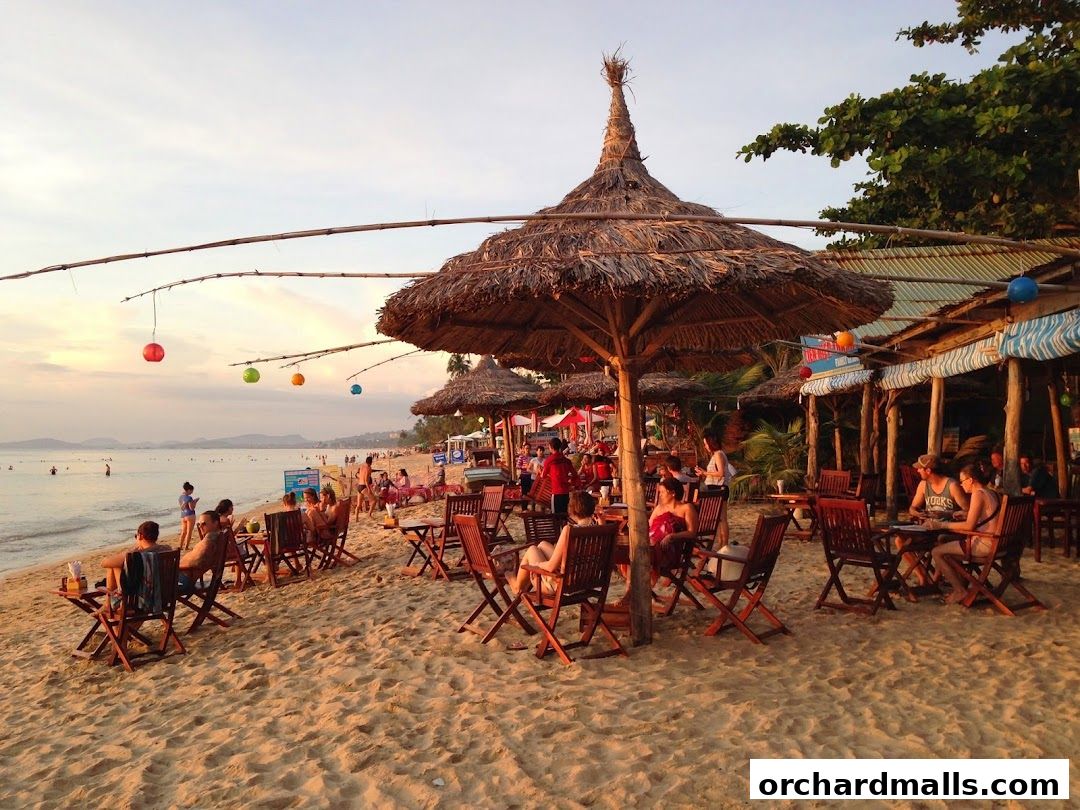 People relaxing at a beachside cafe with thatched umbrellas and tables.