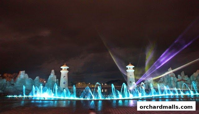 A nighttime view of a water fountain show with lighthouses and laser lights.