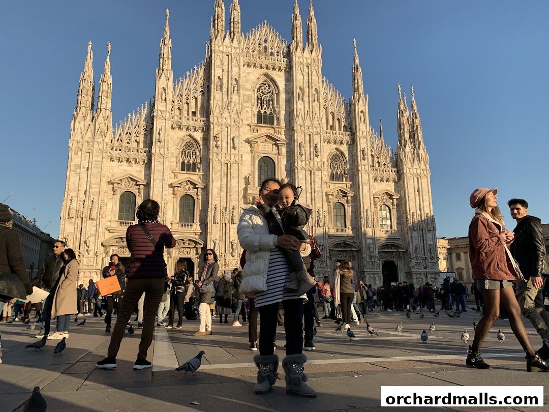 People gather in front of a grand cathedral, with some holding children and others taking photos.