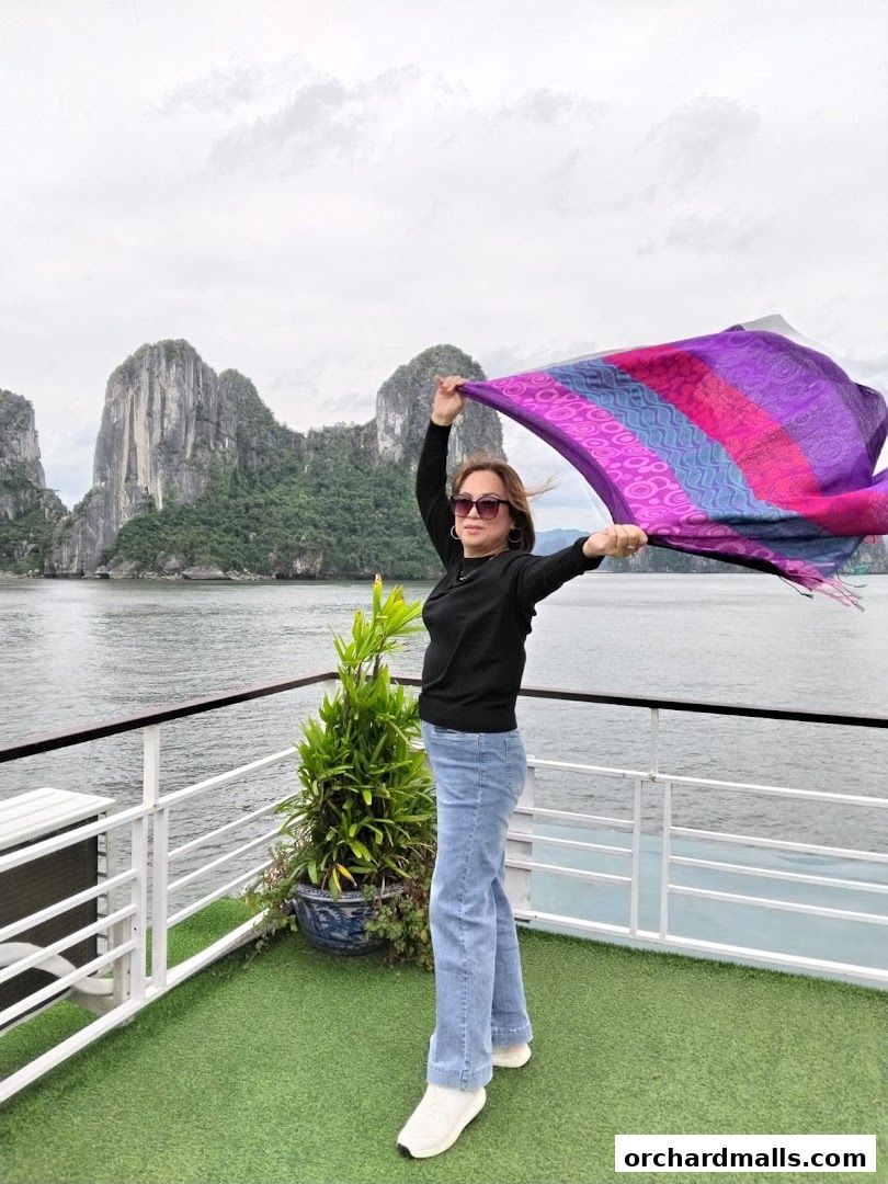 A woman with a colorful scarf stands on a deck with a scenic view of limestone karsts.