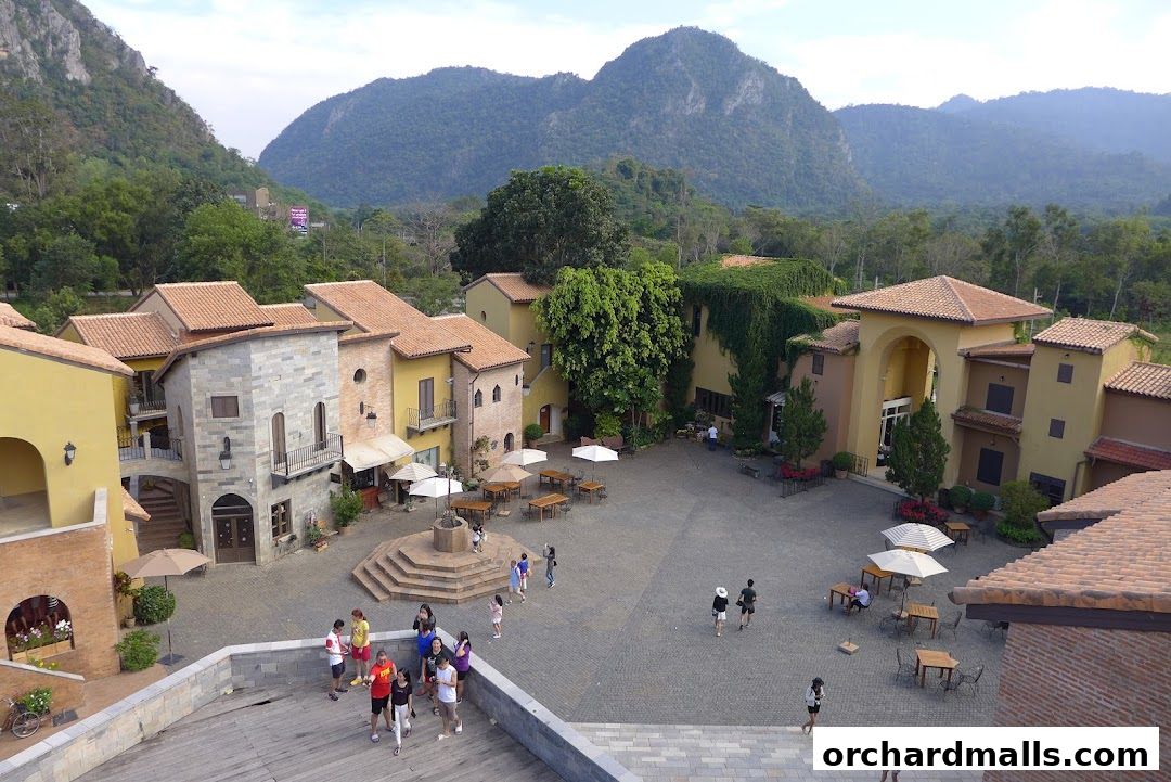 A picturesque Italian-style village square with shops and people enjoying the outdoors.