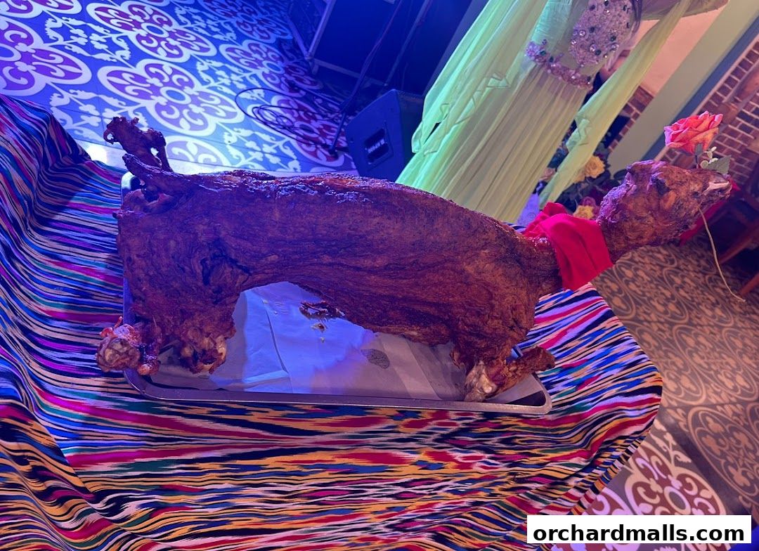 A whole roasted lamb presented on a platter with colorful fabric and a rose.