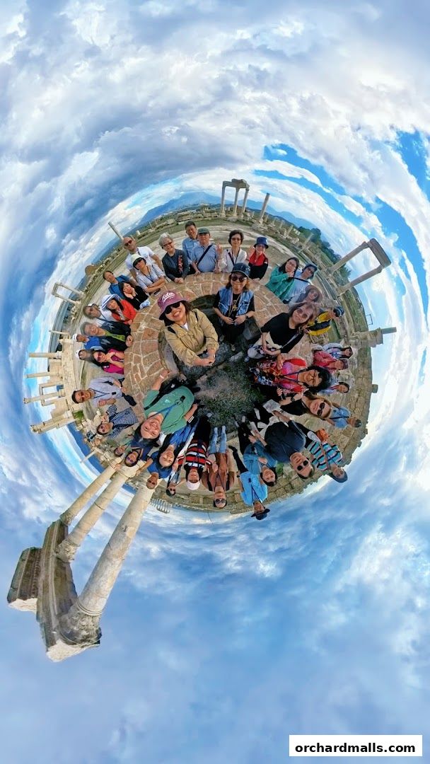 A group of tourists poses for a panoramic photo at an ancient archaeological site.