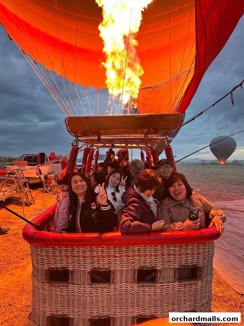 People smiling and posing in a hot air balloon basket with a flame igniting.