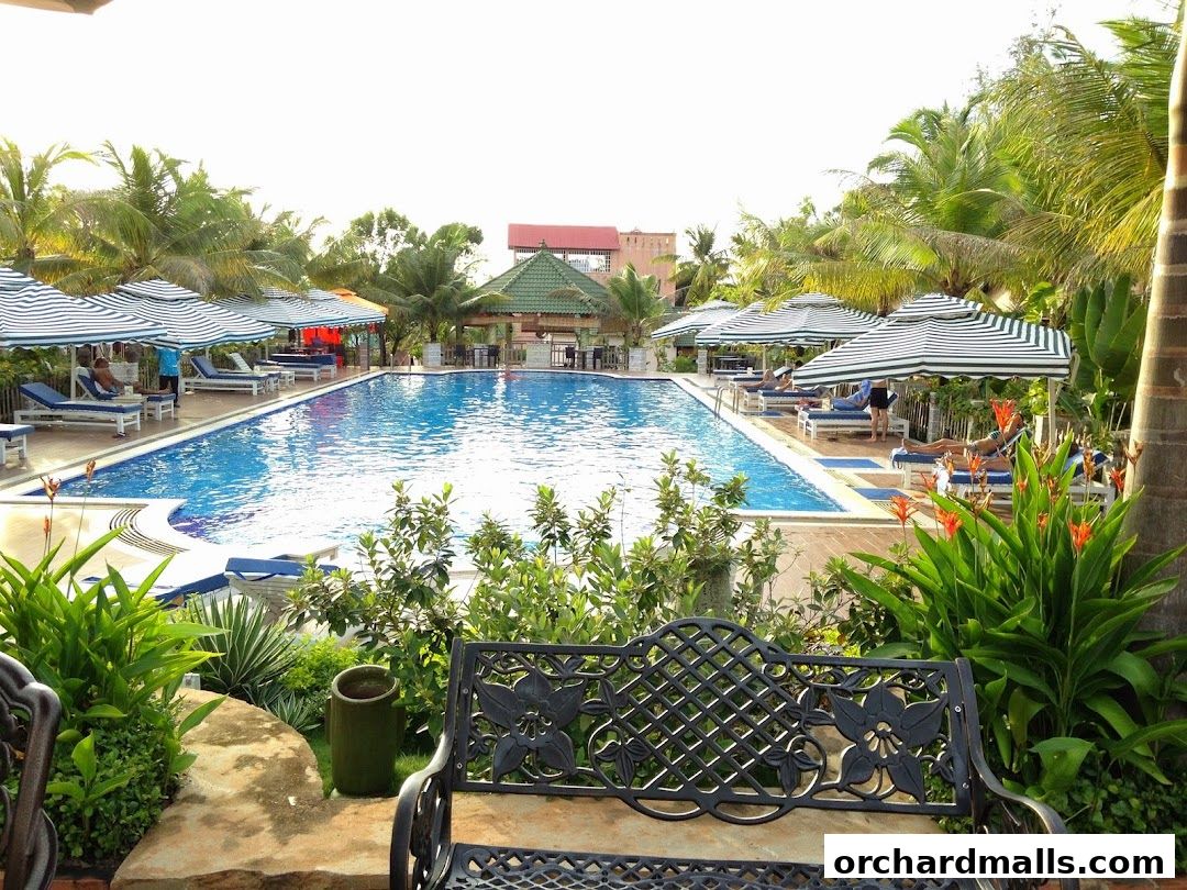 A resort-style swimming pool with lounge chairs and umbrellas, surrounded by lush greenery.