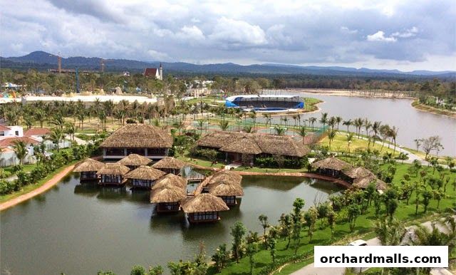 Aerial view of a resort with thatched-roof bungalows on a lake and surrounding greenery.