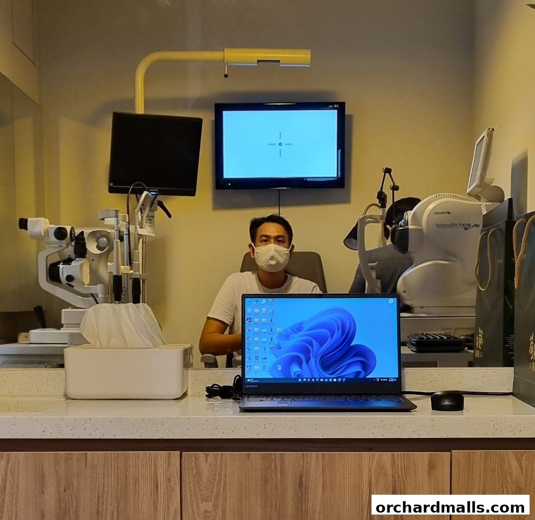 An optometrist wearing a mask sits at a desk with eye examination equipment.