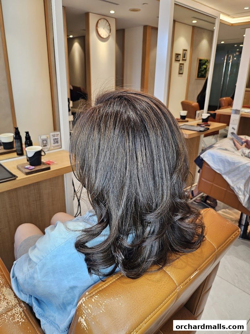 A person sits in a salon chair with styled, layered brown hair.
